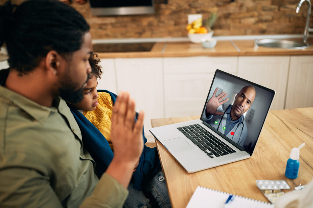 Father and daughter greeting their family doctor during video call over laptop.